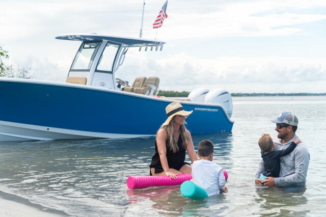 Family with young children swimming and playing at a sandbar near a blue and white center console boat