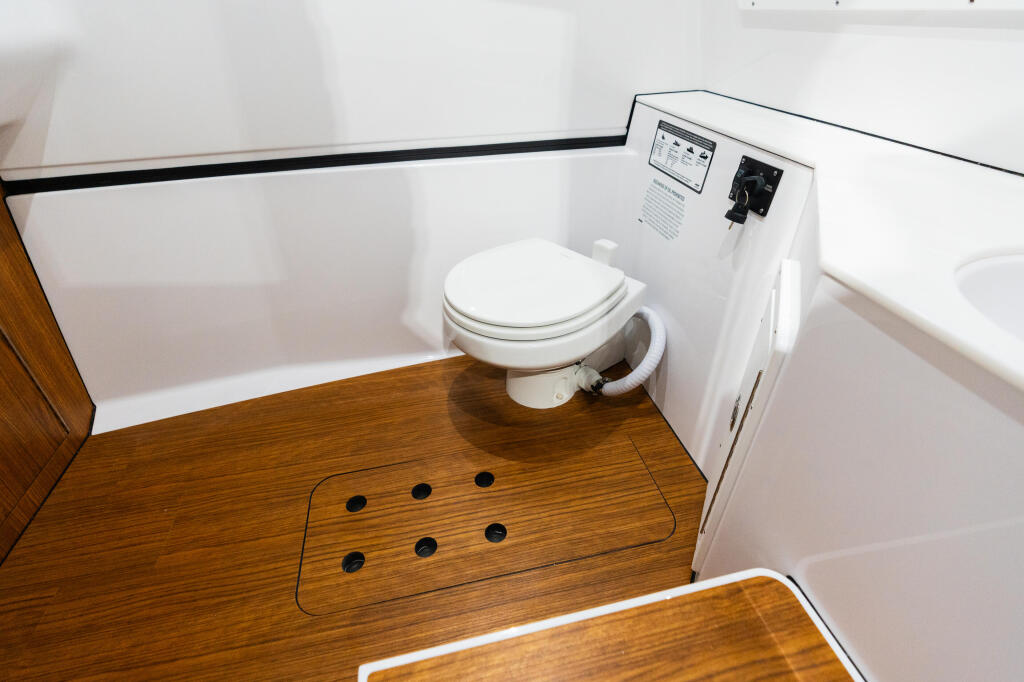 Boat cabin head with white ceramic toilet, wood flooring, and digital control panel mounted on wall