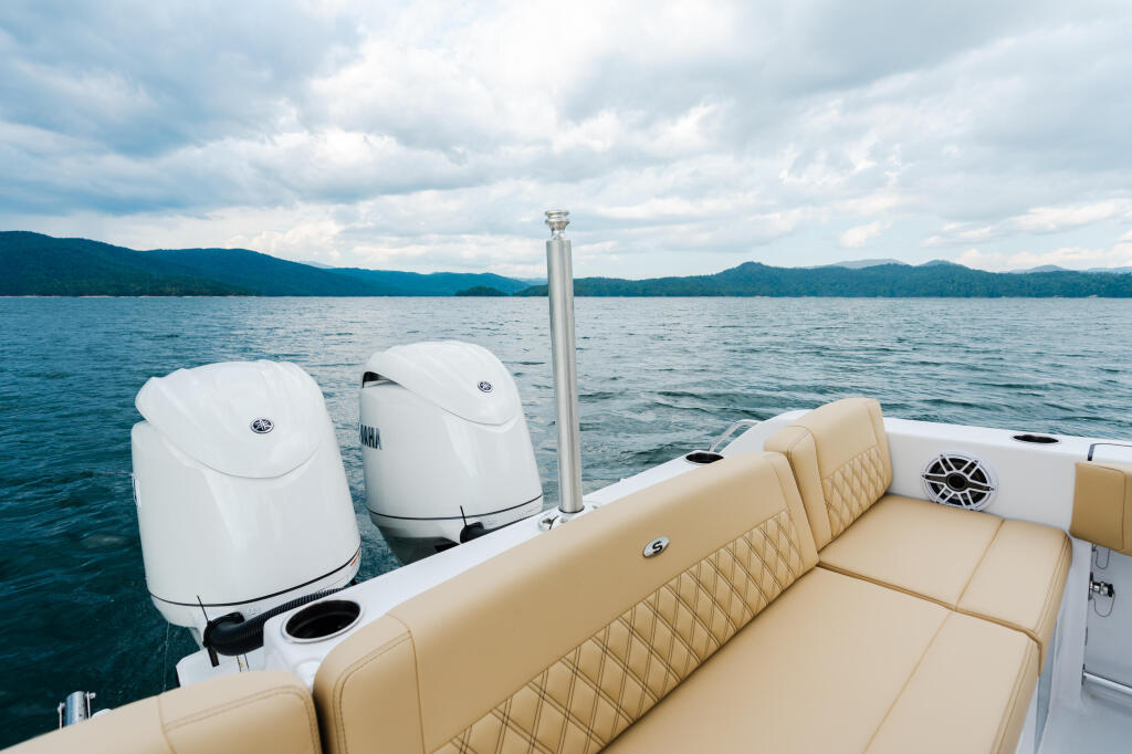 Cream-colored boat seating and twin outboard engines on a lake with forested mountains in the background