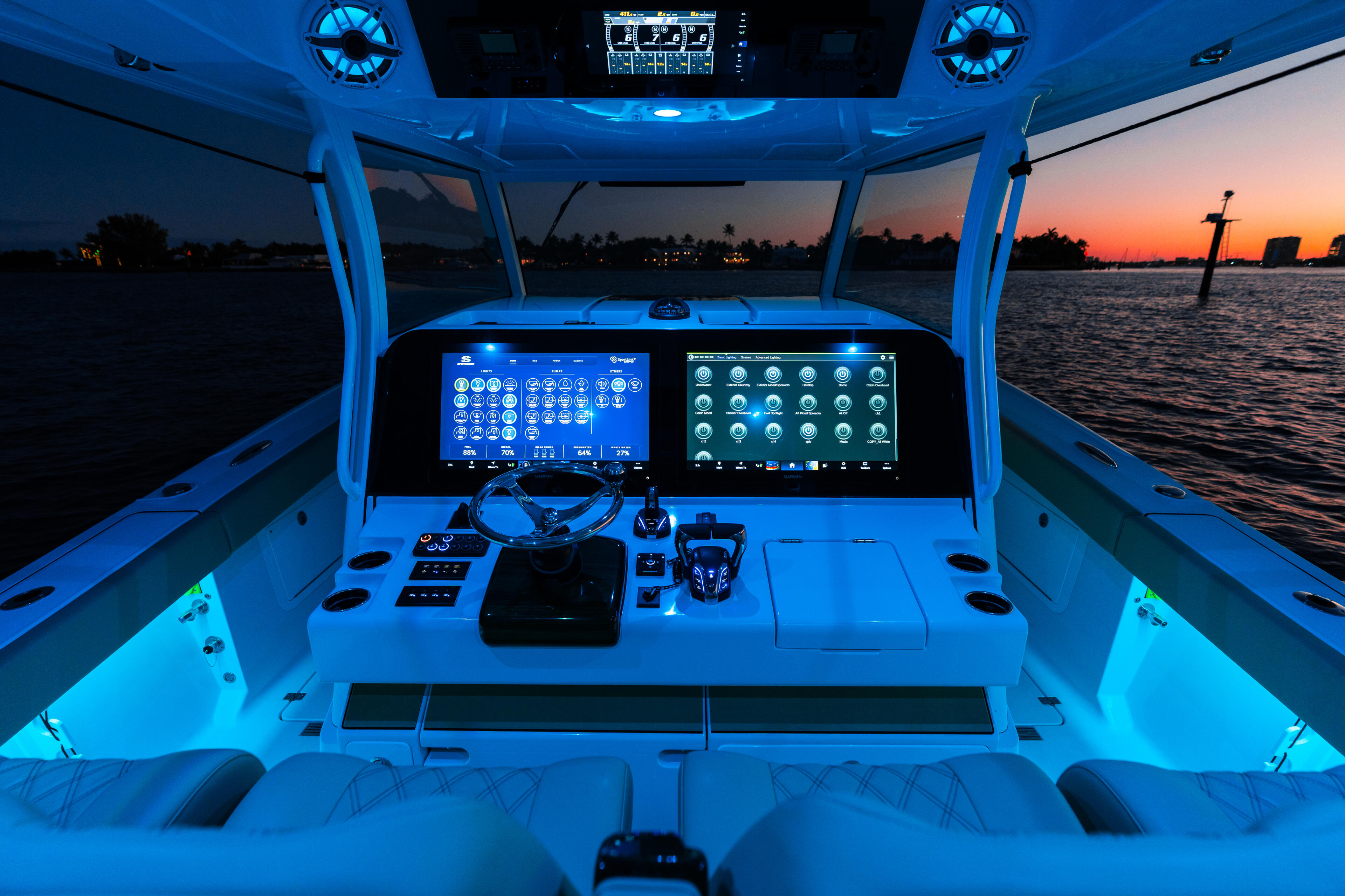 Center console helm with dual display screens and RGB ambient lighting at sunset, boat docked with water and treeline visible
