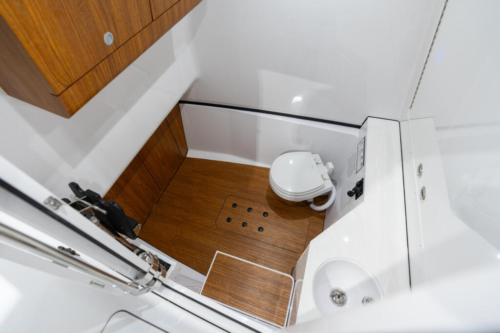 Overhead view of boat cabin bathroom with wood flooring, white walls, toilet, and sink fixtures