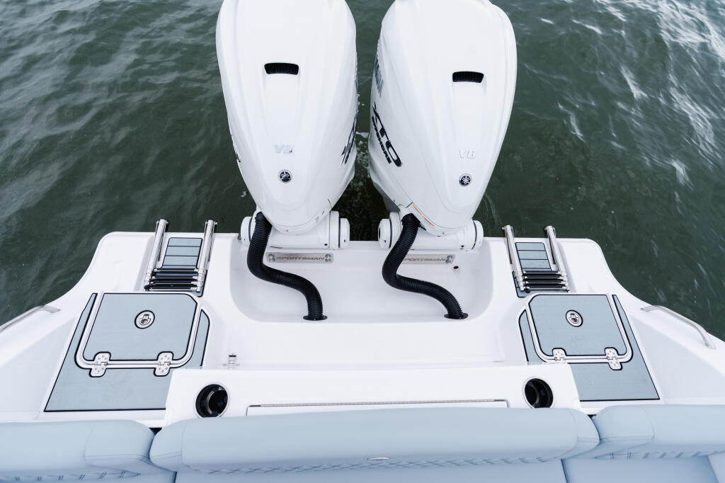 Overhead view of dual outboard engines with control systems and storage compartments on a white center console boat
