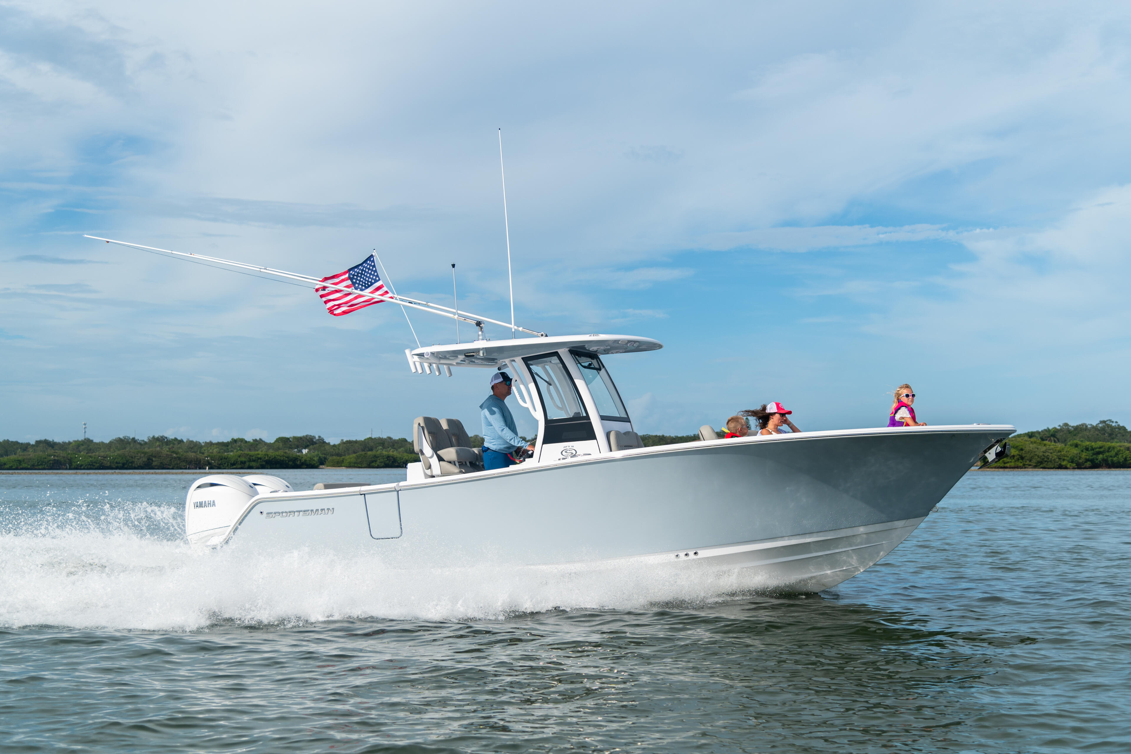 White center console boat with hard-top running in shallow water near a sandbar, American flag flying, passengers enjoying a day on the water