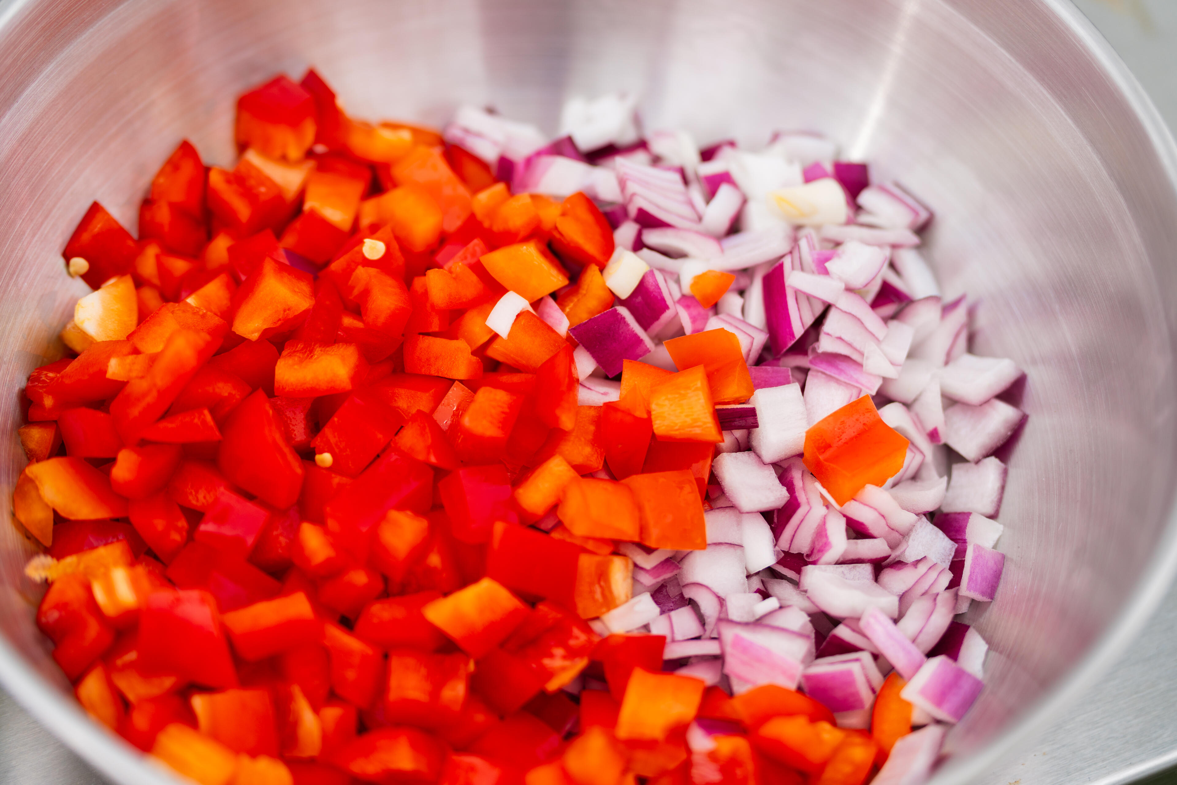 Diced red bell peppers and purple onions in a stainless steel bowl