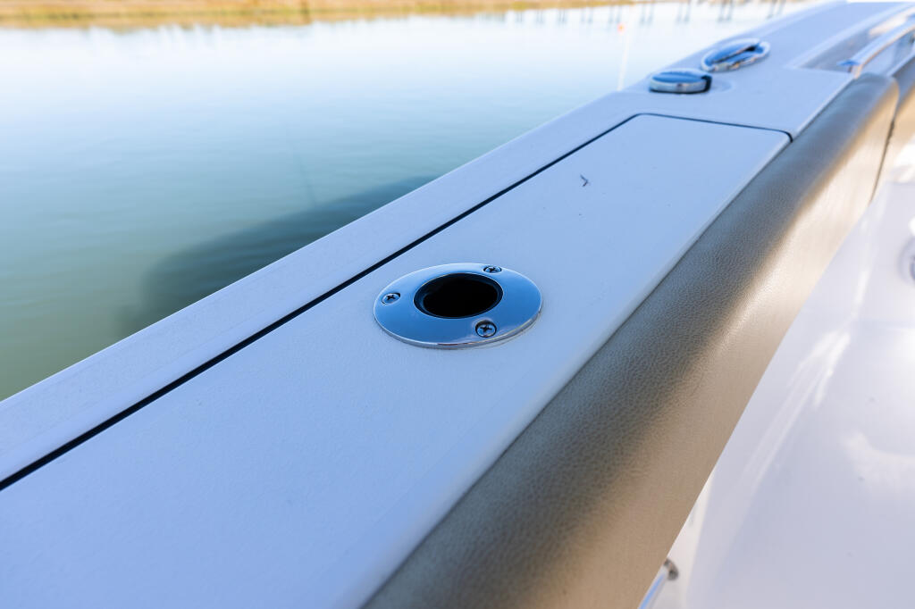 Close-up of a blue flush-mount gunwale rod holder on a boat's side rail near calm water
