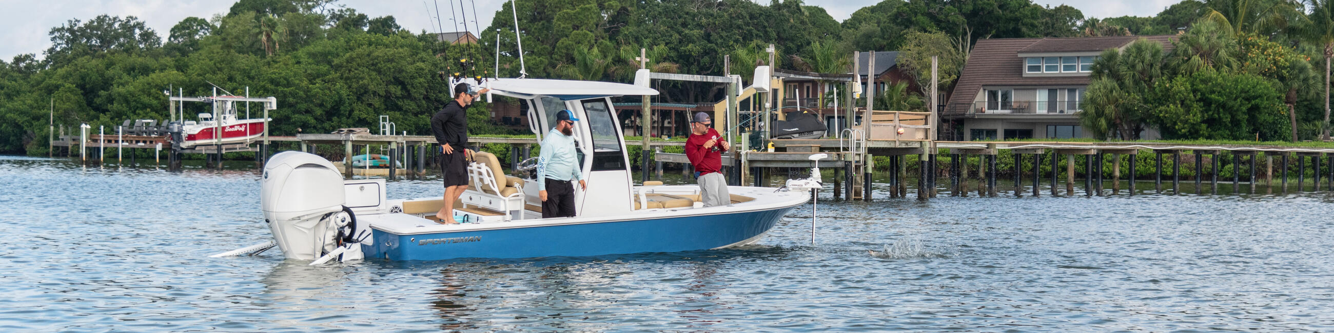 Blue and white fishing boat with passengers cruising past waterfront homes in a calm bay