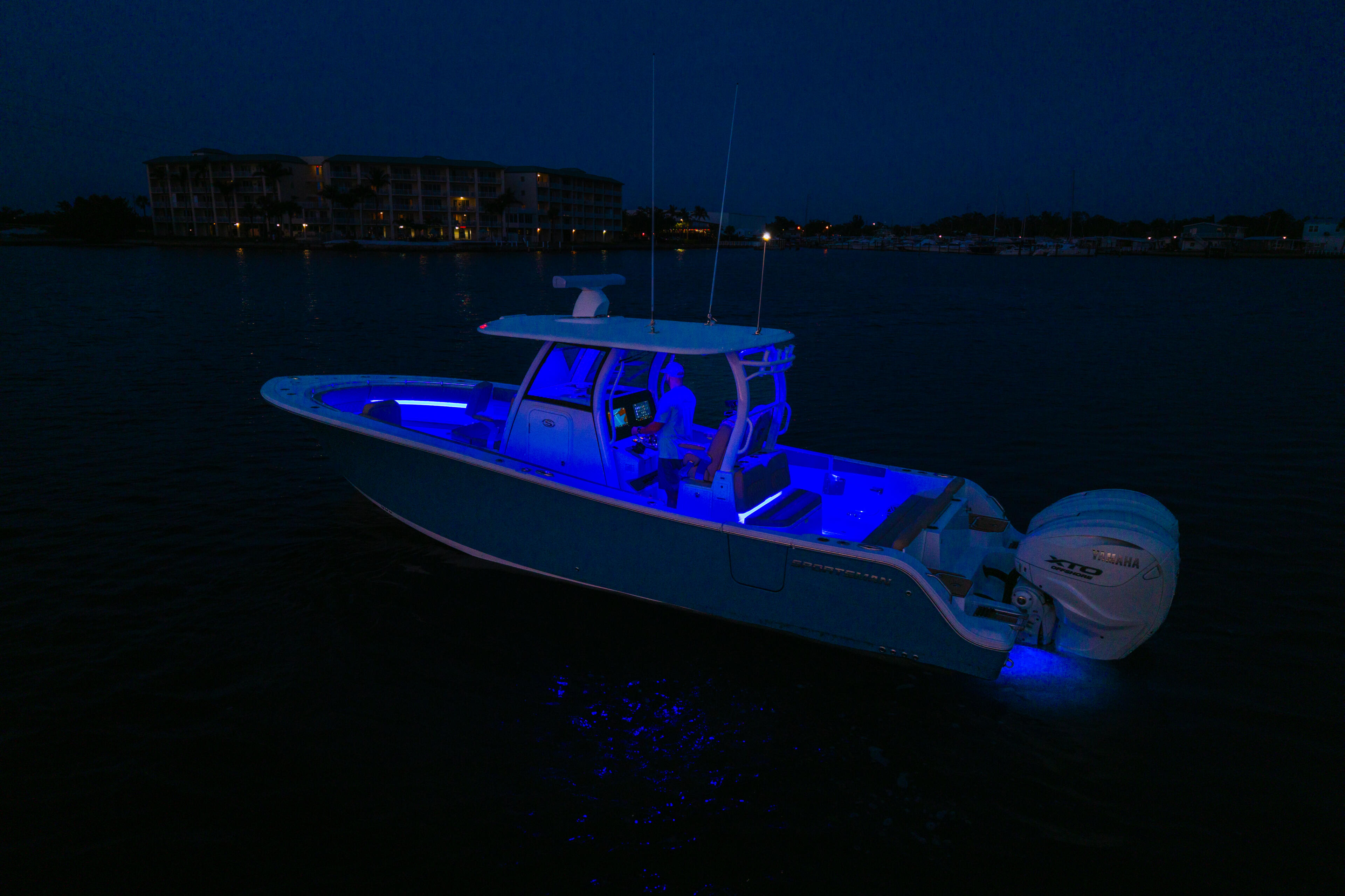 Fishing boat illuminated by blue LED lighting at dusk in a calm marina