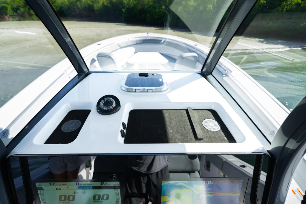 Helm station with compass, electronics displays, and windshield view of calm water and forested shoreline