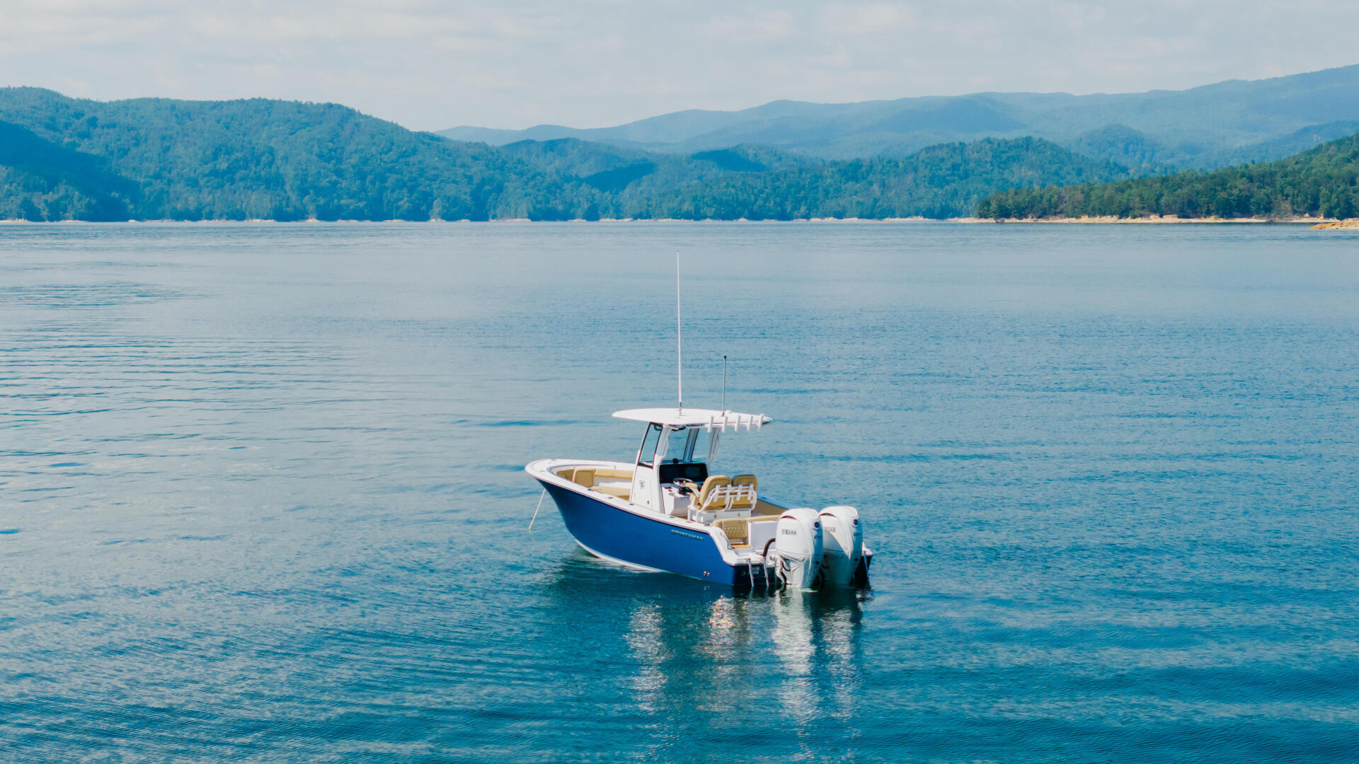 Blue and white boat anchored in calm clear water with forested mountains in the background