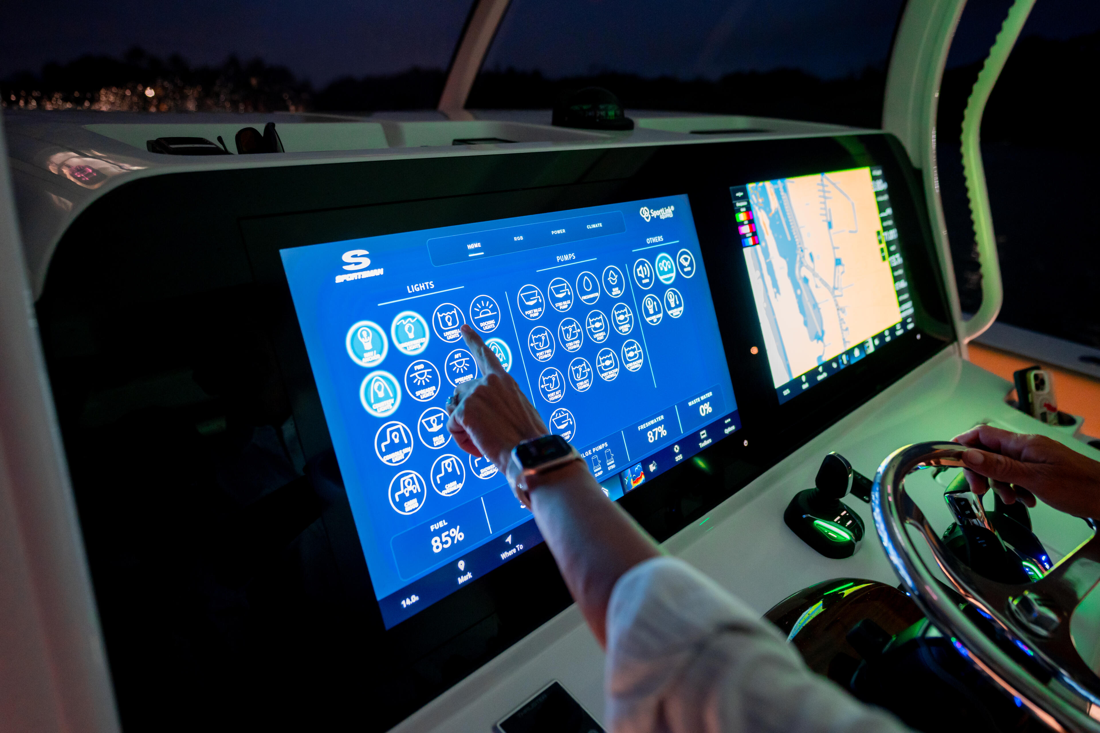 Hand touching illuminated touchscreen control panel at boat helm during evening cruise
