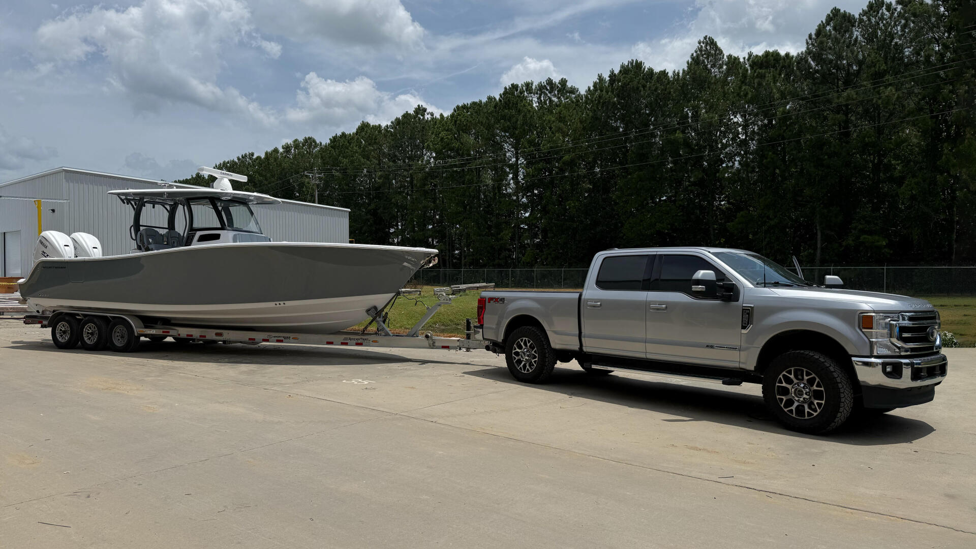Silver pickup truck towing a large center console fishing boat on a triple-axle trailer at a marina facility