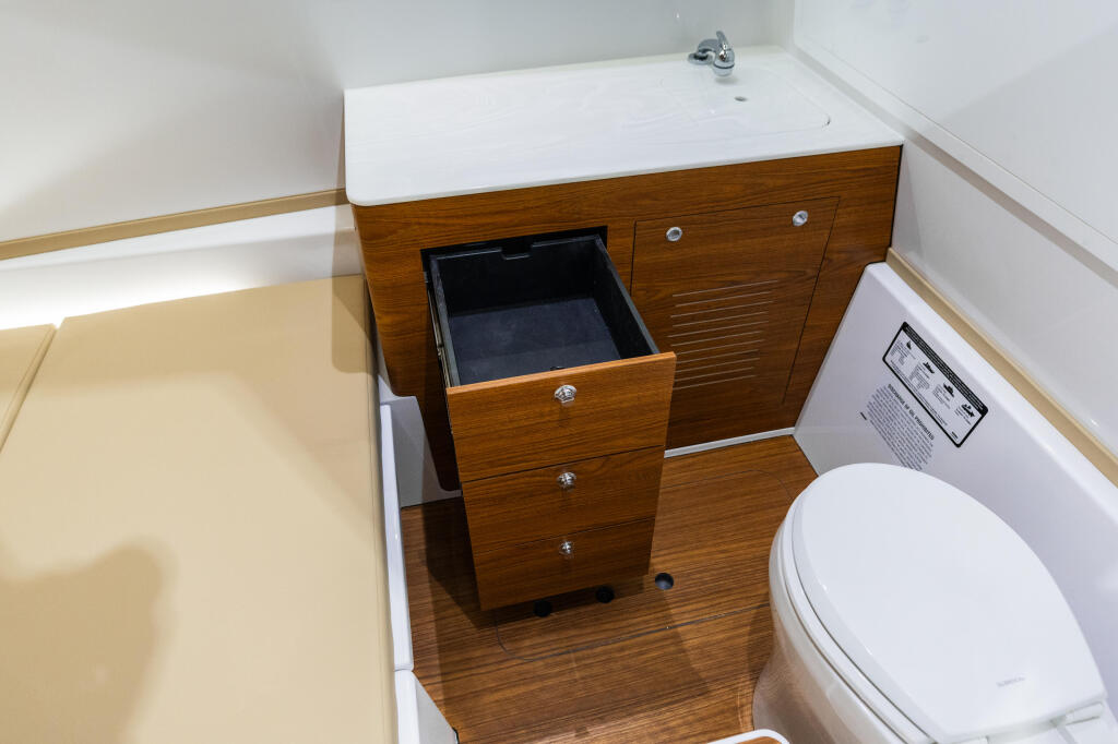 Compact cabin bathroom with wood cabinetry, white sink, toilet, and open storage drawer