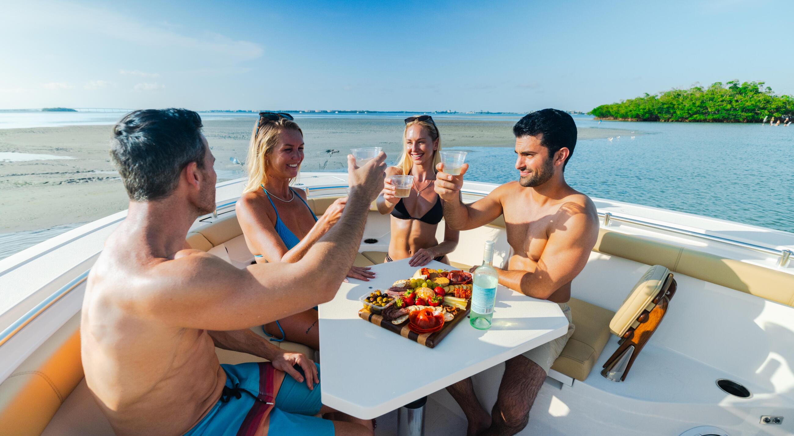 Four friends enjoying drinks and appetizers while relaxing aboard a boat anchored near a sandy beach and mangroves