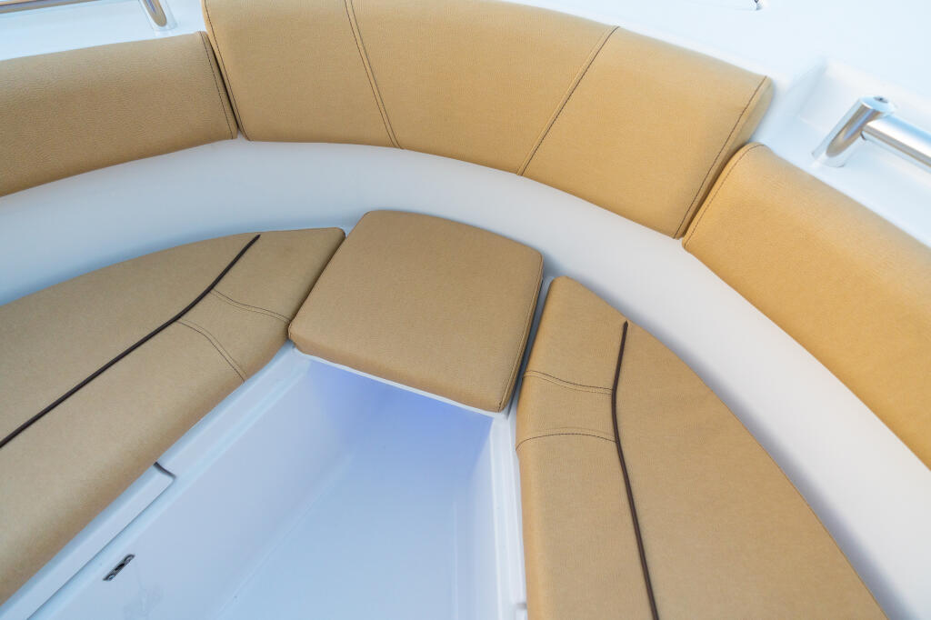 Tan upholstered seating with curved white railings and removable cushioned filler board in boat cabin