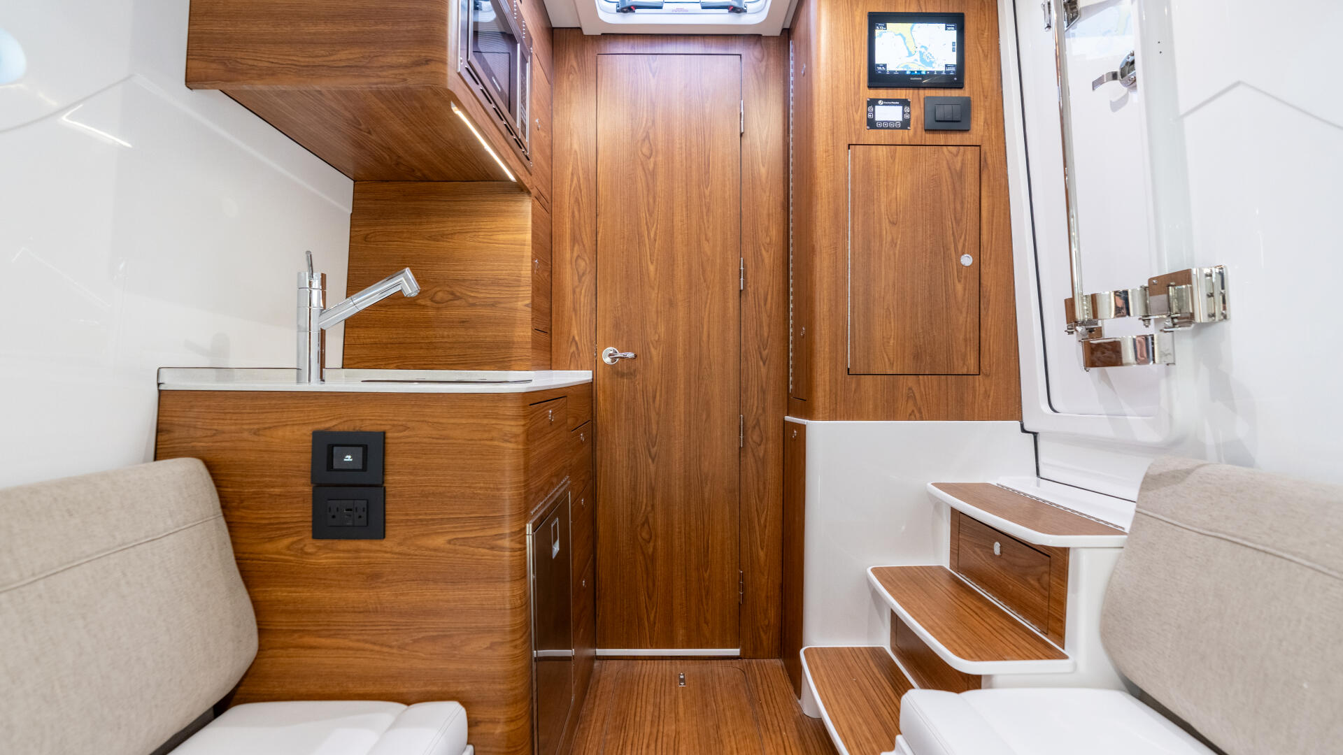 Boat cabin interior with wood cabinetry, seating berths, galley sink, and skylight overhead