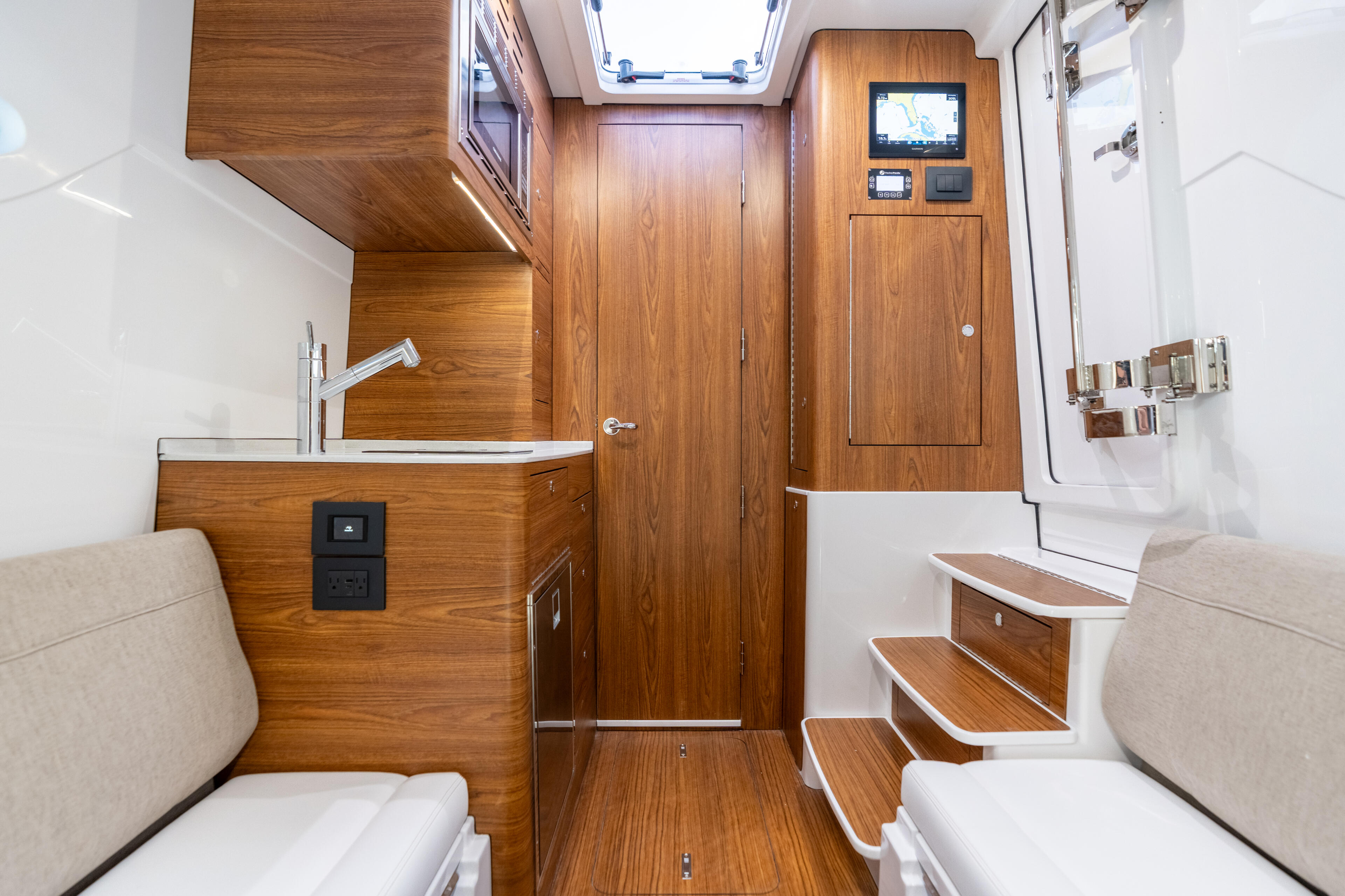 Boat cabin interior with wood cabinetry, seating berths, galley sink, and skylight overhead