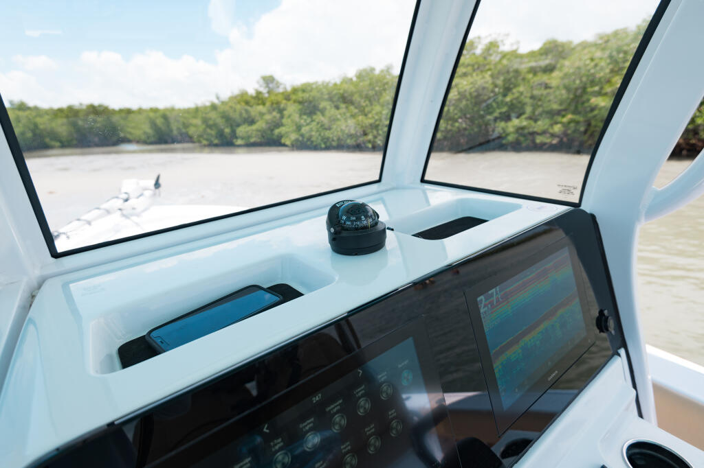 Boat helm console with dual displays, compass, and windshield overlooking mangrove waterway