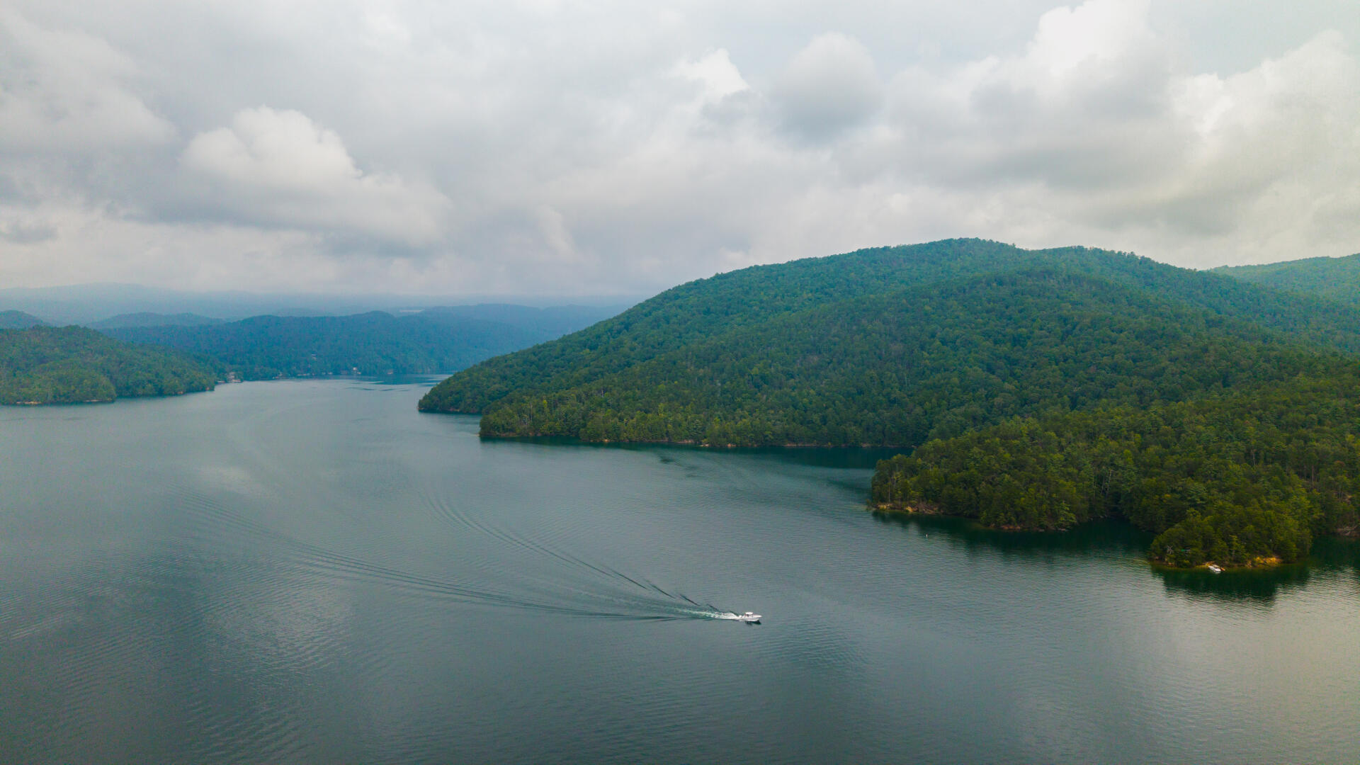 Speedboat cruising through a forested mountain lake with emerald hills rising on both sides
