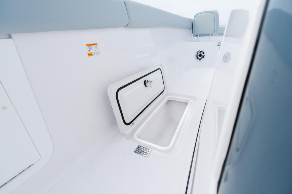 Open livewell and storage compartment on white boat deck with speakers and cabin seating visible