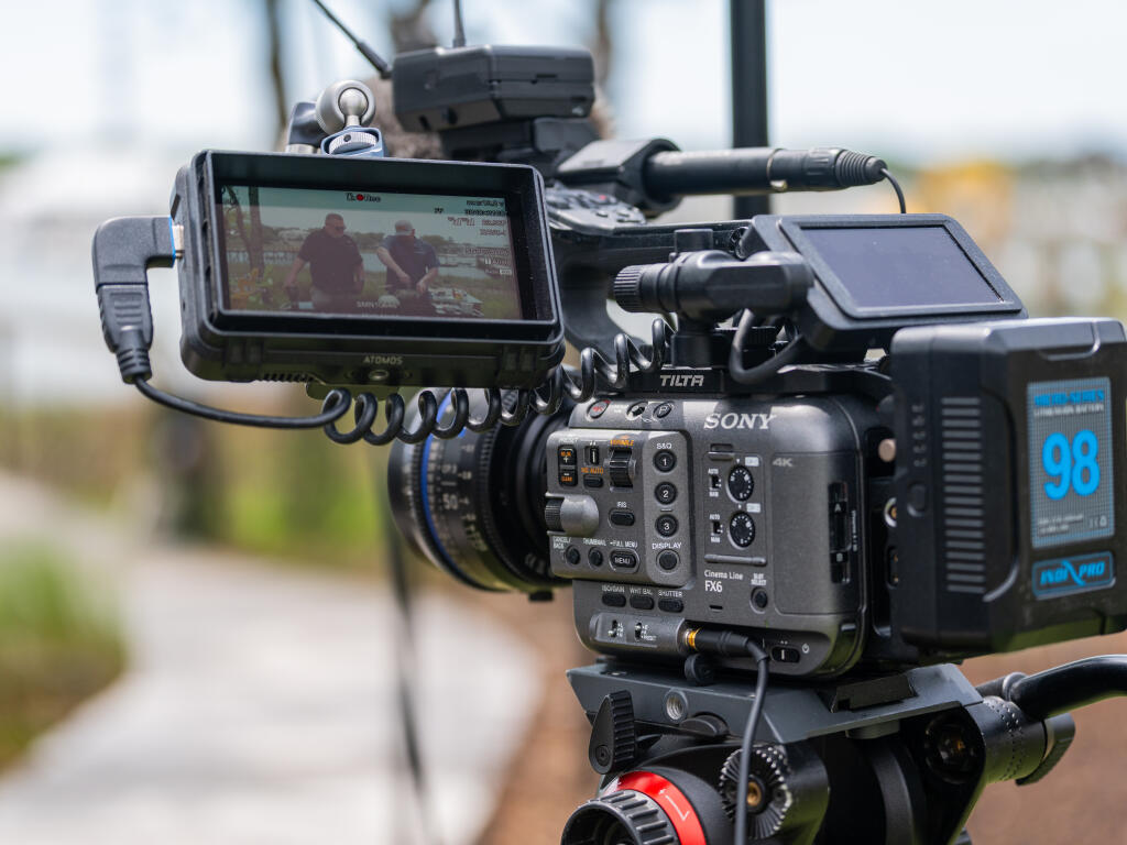 Professional Sony cinema camera with external monitor and audio equipment mounted on tripod at marina location