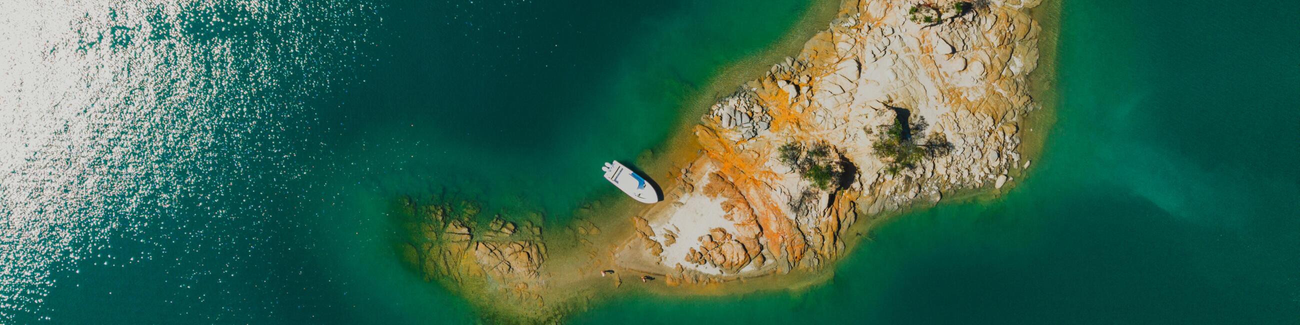 Aerial view of a small fishing boat anchored in clear turquoise water next to a rocky island outcropping