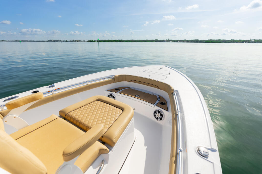 Bow seating area with tan quilted cushions and white fiberglass hull on calm bay water