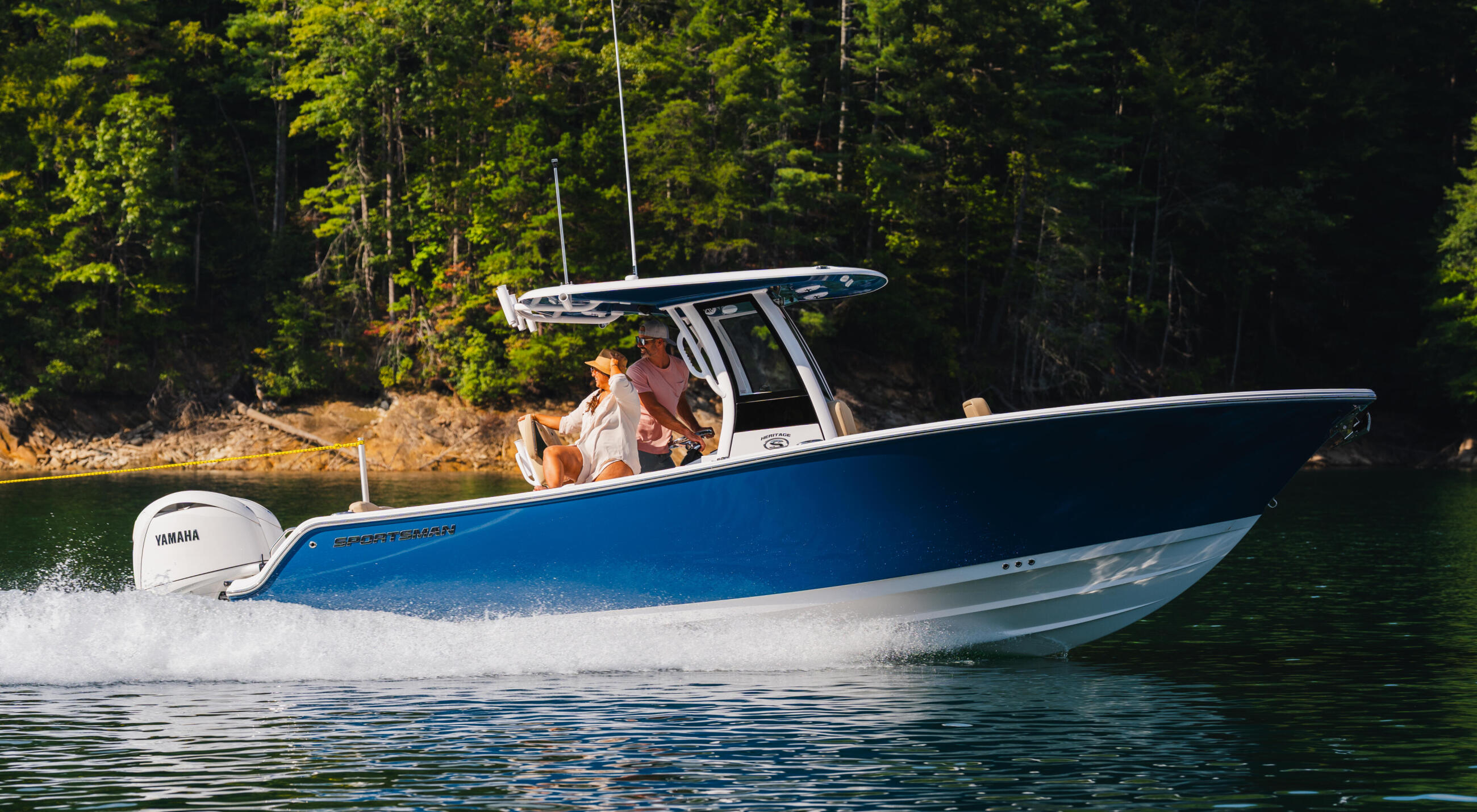 Blue and white center console boat with hard-top running at speed on a lake surrounded by dense forest
