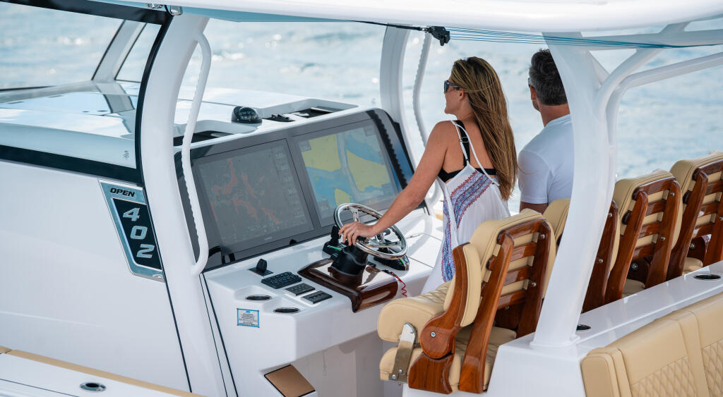Woman at helm with Garmin electronics and man in cabin with tan seating and hard-top