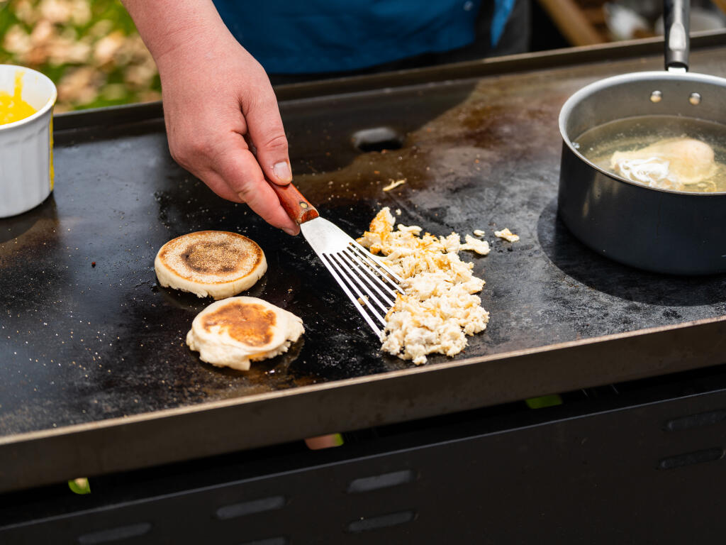 Hand using a fork to break apart crab cakes on a flat-top griddle during outdoor boat cooking
