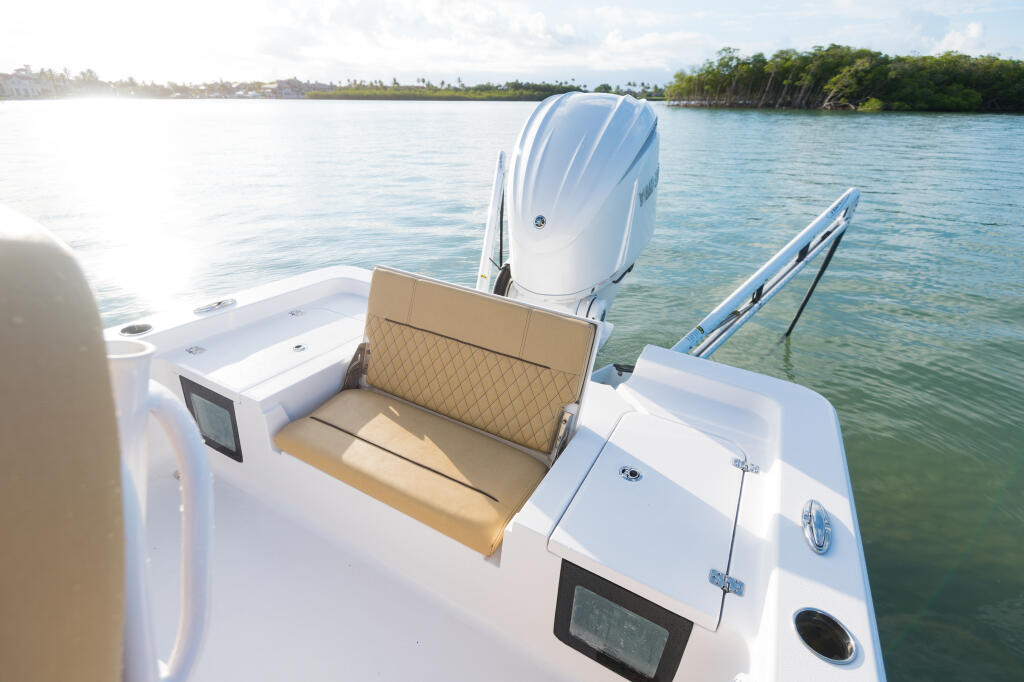 Rear deck of white boat with tan fold-up bench seat and outboard engine, anchored in turquoise tropical waters
