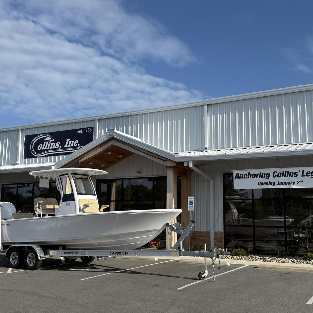 White center console boat on trailer displayed outside Collins, Inc. marina showroom with blue sky overhead