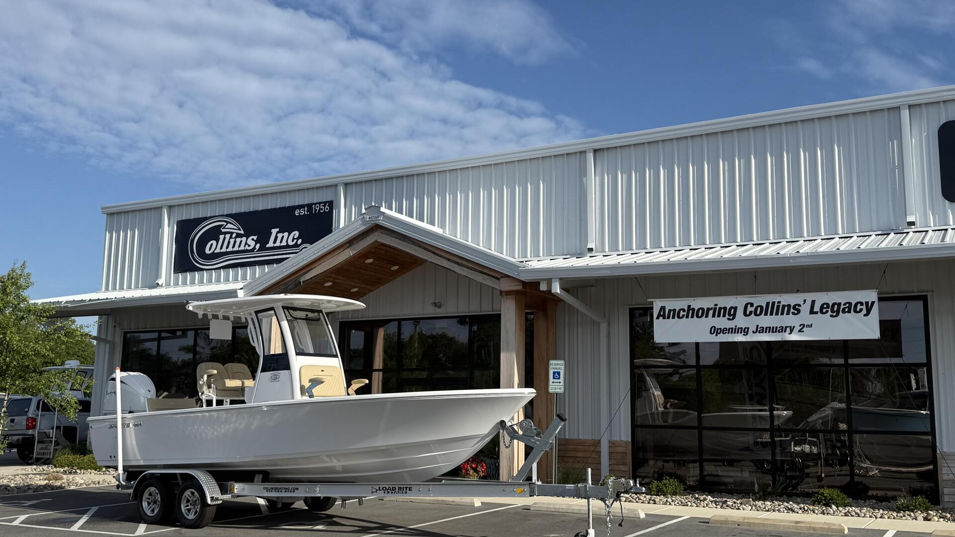 White center console boat on trailer displayed outside Collins, Inc. marina showroom with blue sky overhead
