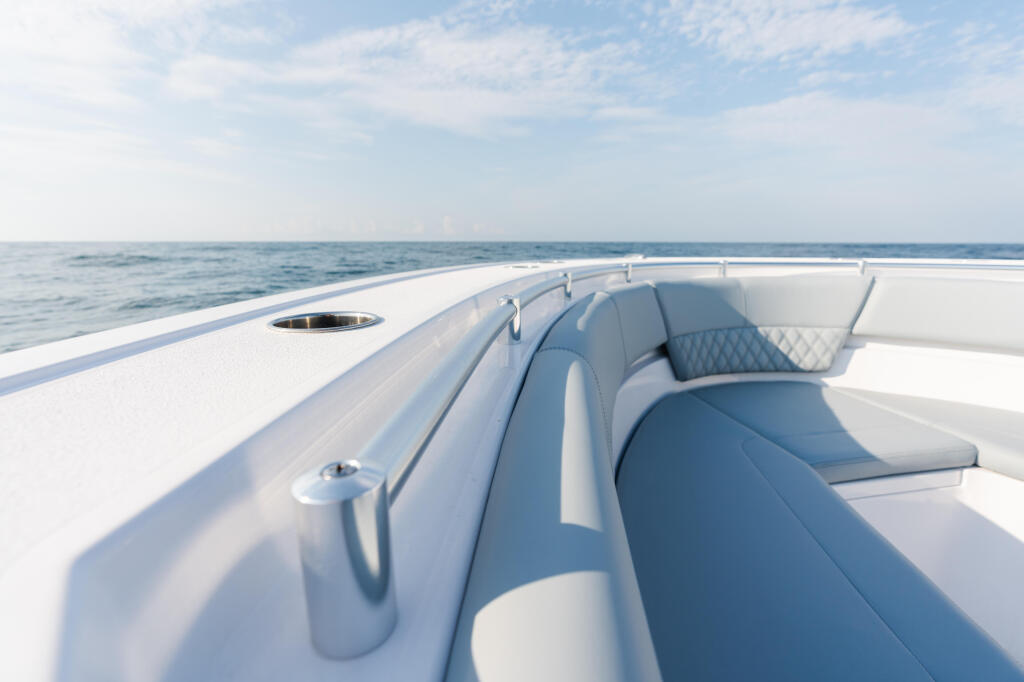 Blue and white cushioned seating along the gunwale of a boat cruising offshore with calm ocean and sky in background