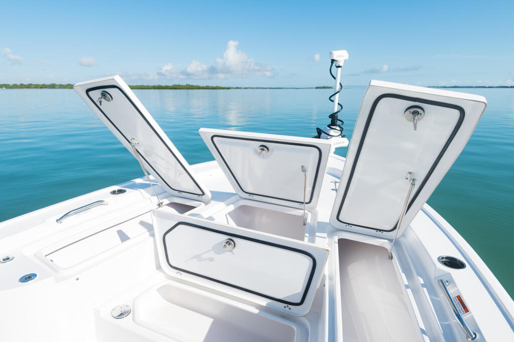 Multiple white storage compartments and hatch covers on the bow of a bay boat with calm water and clear sky
