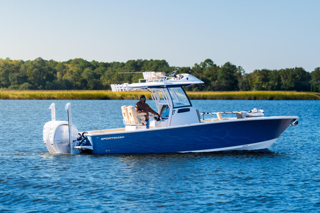 Blue and white Sportsman bay boat with hard-top running in calm water near marsh shoreline