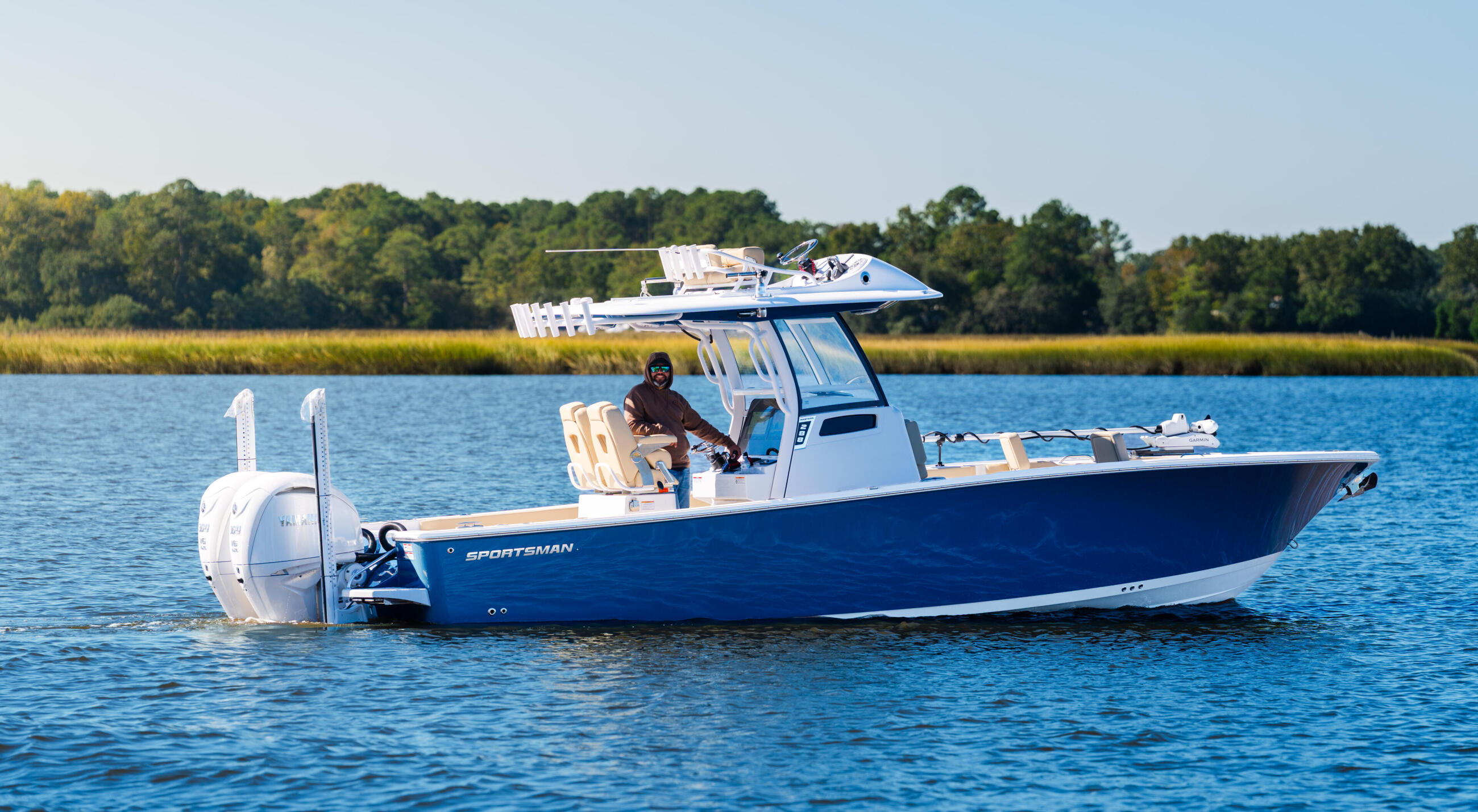 Blue and white Sportsman bay boat with hard-top running in calm water near marsh shoreline