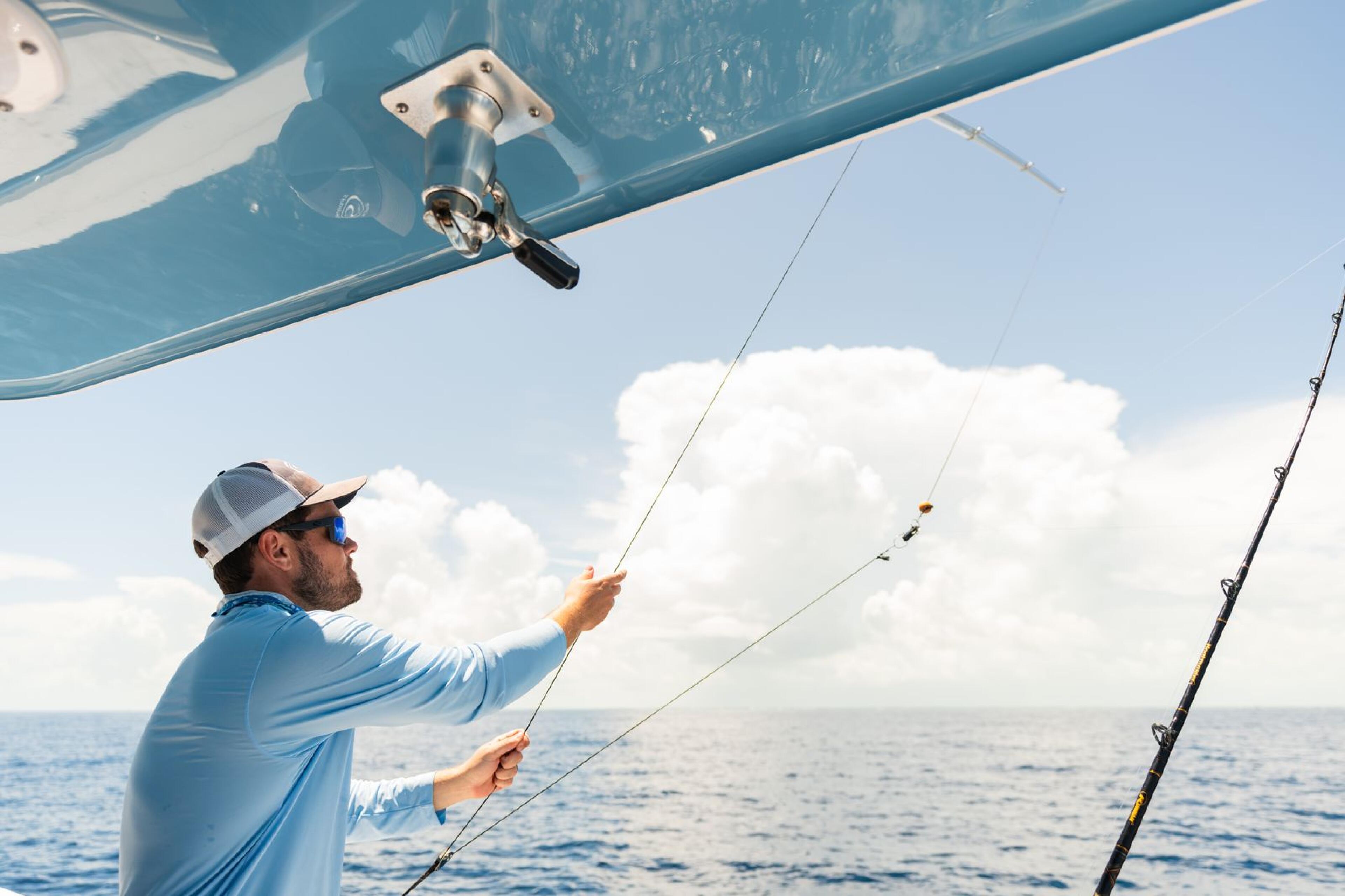Angler in blue shirt holding fishing rod while standing on offshore boat under blue sky with white clouds