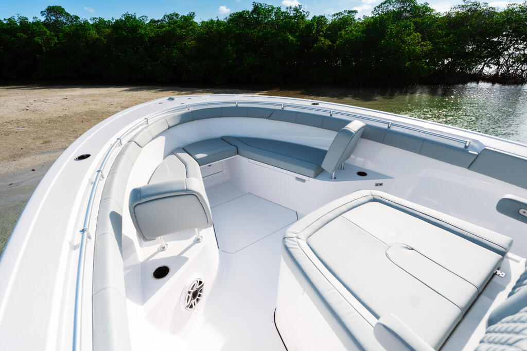 Spacious open cockpit with white upholstered seating and storage, docked at a sandy beach near mangroves