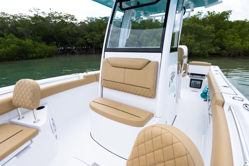 Helm station and comfortable seating area of a white center console boat with tan upholstery overlooking mangrove coastline