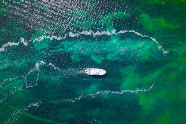 Aerial view of white boat anchored in turquoise waters near a shallow sandbar with breaking waves