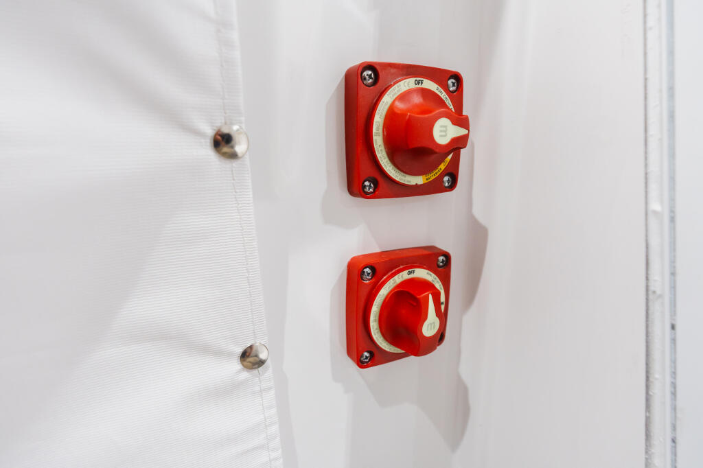 Two red battery selector switches mounted on white cabin wall with stainless steel hardware