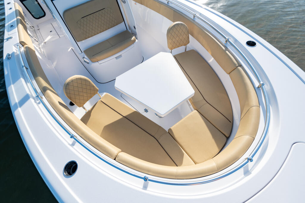 Overhead view of boat's open bow with tan cushioned seating, white table, and cabin access