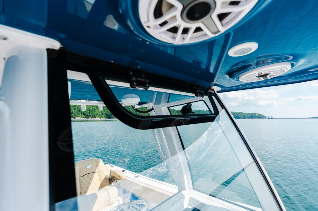 Interior view through boat windshield showing helm area, white railing, and calm lake with forested shoreline
