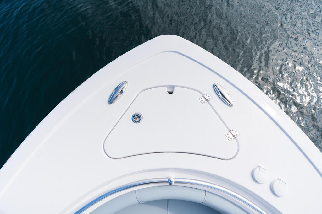 Overhead view of boat bow with windshield, cleats, and compass gauge in calm water