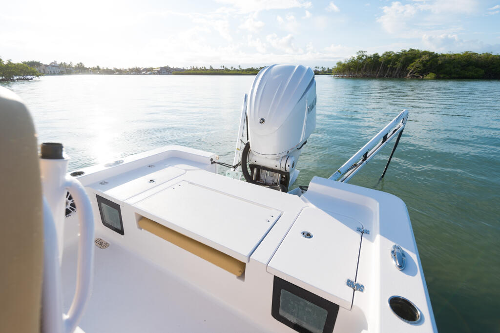 Rear deck of a white center console boat with dual outboard engines, storage compartments, and mangrove shoreline in background