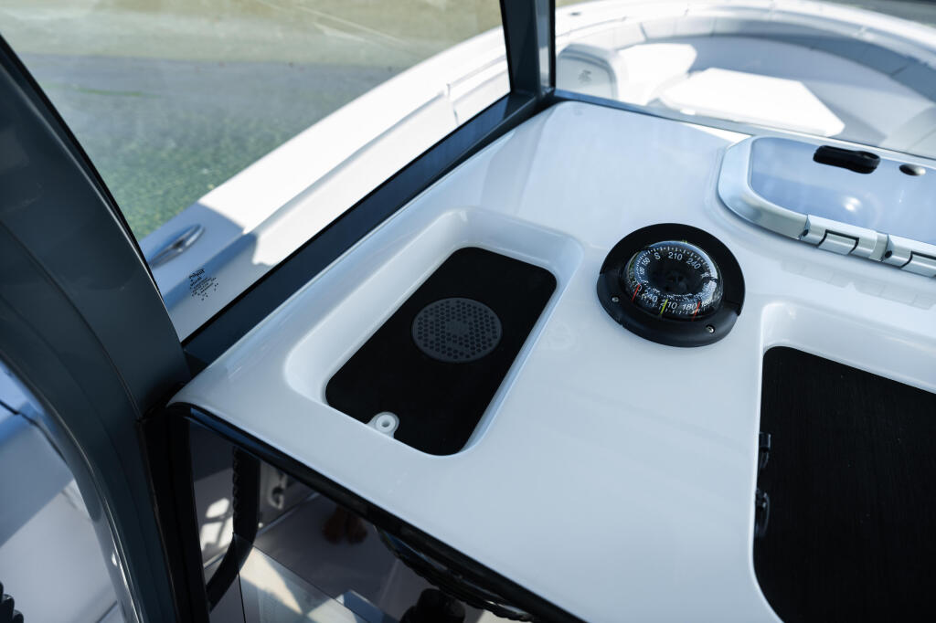 Helm console with compass, speaker, and windshield overlooking calm water
