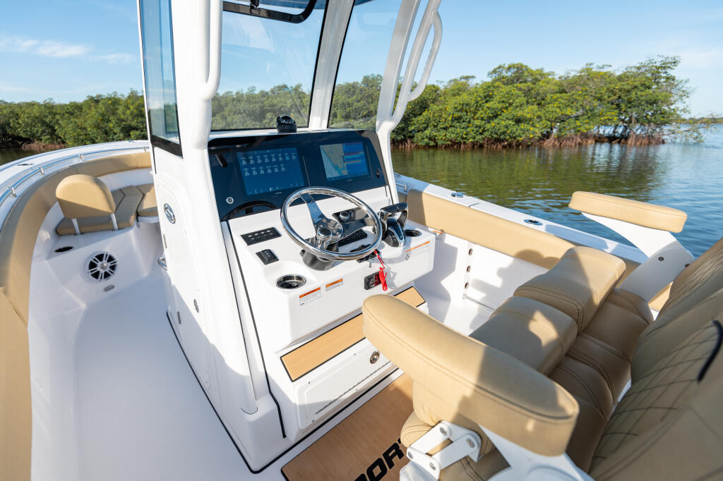 Modern boat helm with dual screens, steering wheel, and tan seating overlooking mangrove shoreline