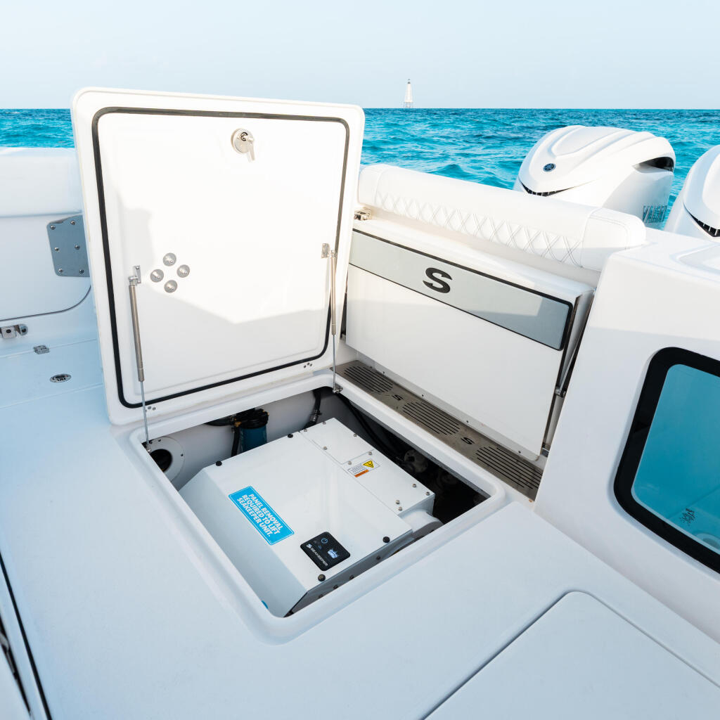 Open storage compartment with electronics and equipment visible inside a white center console boat