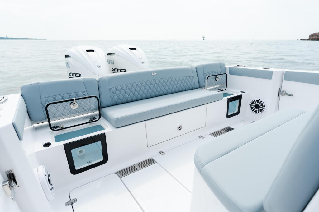 Modern center console boat with gray upholstered seating, dual outboard engines, and electronics display