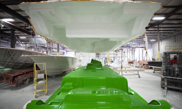 Boat hull under construction in manufacturing facility with green gelcoat finish applied